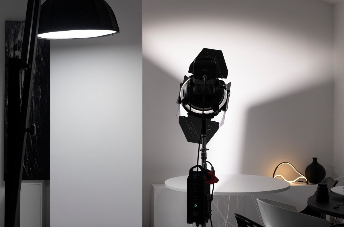Fotoleuchte mit Fluegeltoren auf Stativ leuchtet eine helle Wand an, daneben ein Schirmreflektor — Das Studiozwei, Werbefotograf München