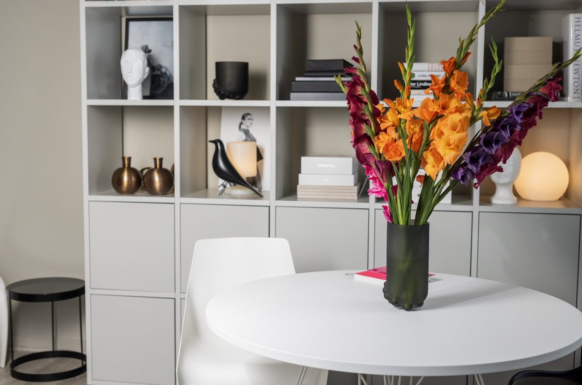 Heller Wohnraum mit weissem Rundtisch und farbenfrohem Gladiolenstrauss vor einem Designregal — Das Studiozwei, Werbefotograf München