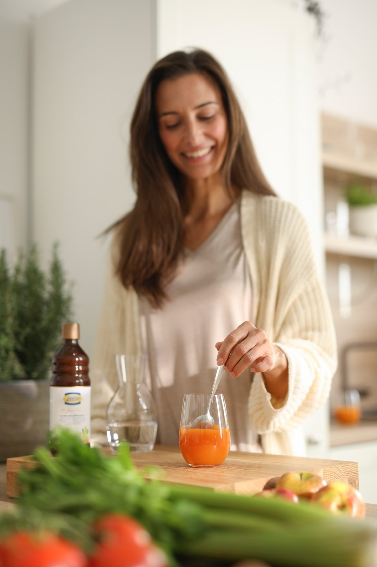 Frau ruehrt in einer hellen Kueche ein Glas mit orangefarbenem Saft an — Das Studiozwei, Werbefotograf München