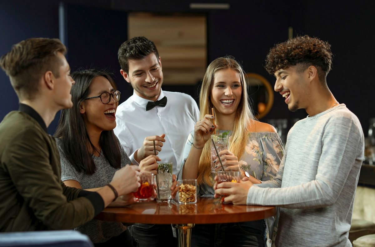 Fuenf junge Menschen lachen gemeinsam an einem Bartisch mit Cocktails — Das Studiozwei, Werbefotograf München