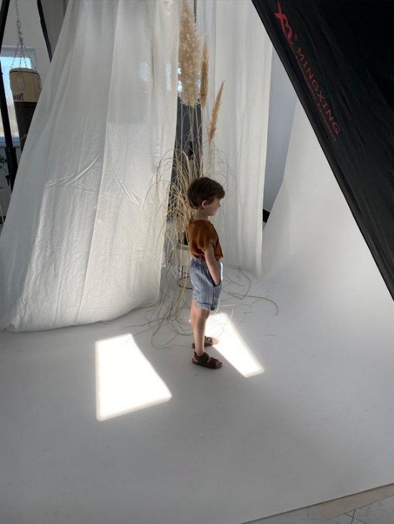 Kleiner Junge auf weisser Hohlkehle neben Pampasgras und Stoffbahnen im Studio — Das Studiozwei, Werbefotograf München