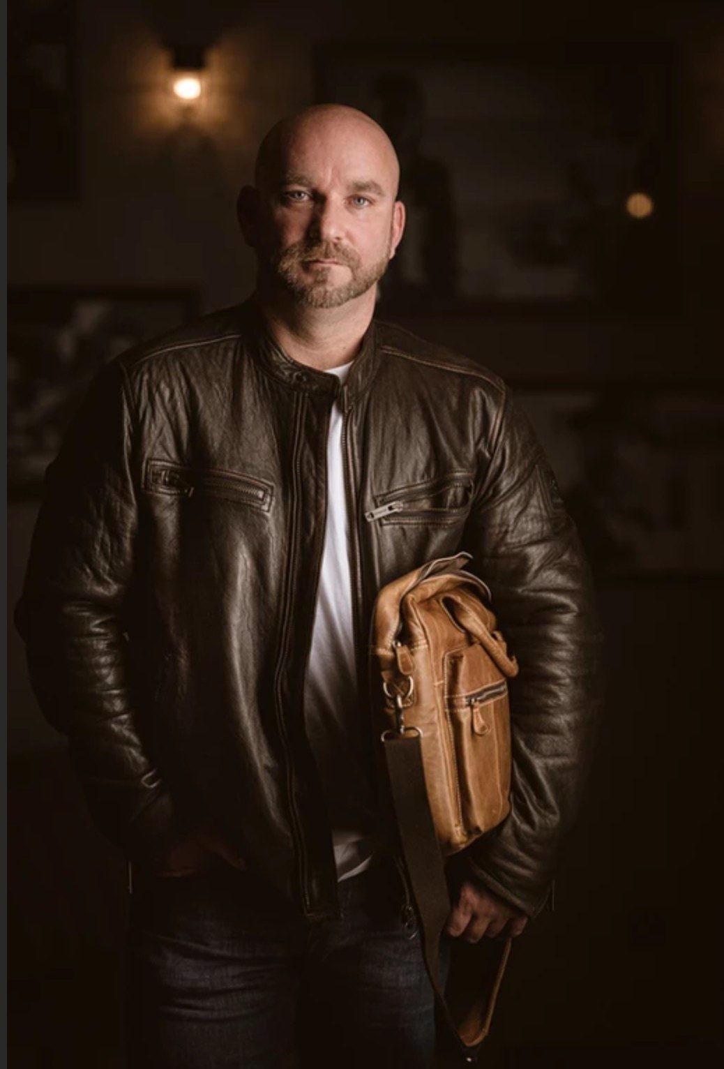 Mann in brauner Lederjacke mit Ledertasche unter dem Arm in warm beleuchtetem Raum — Das Studiozwei, Werbefotograf München