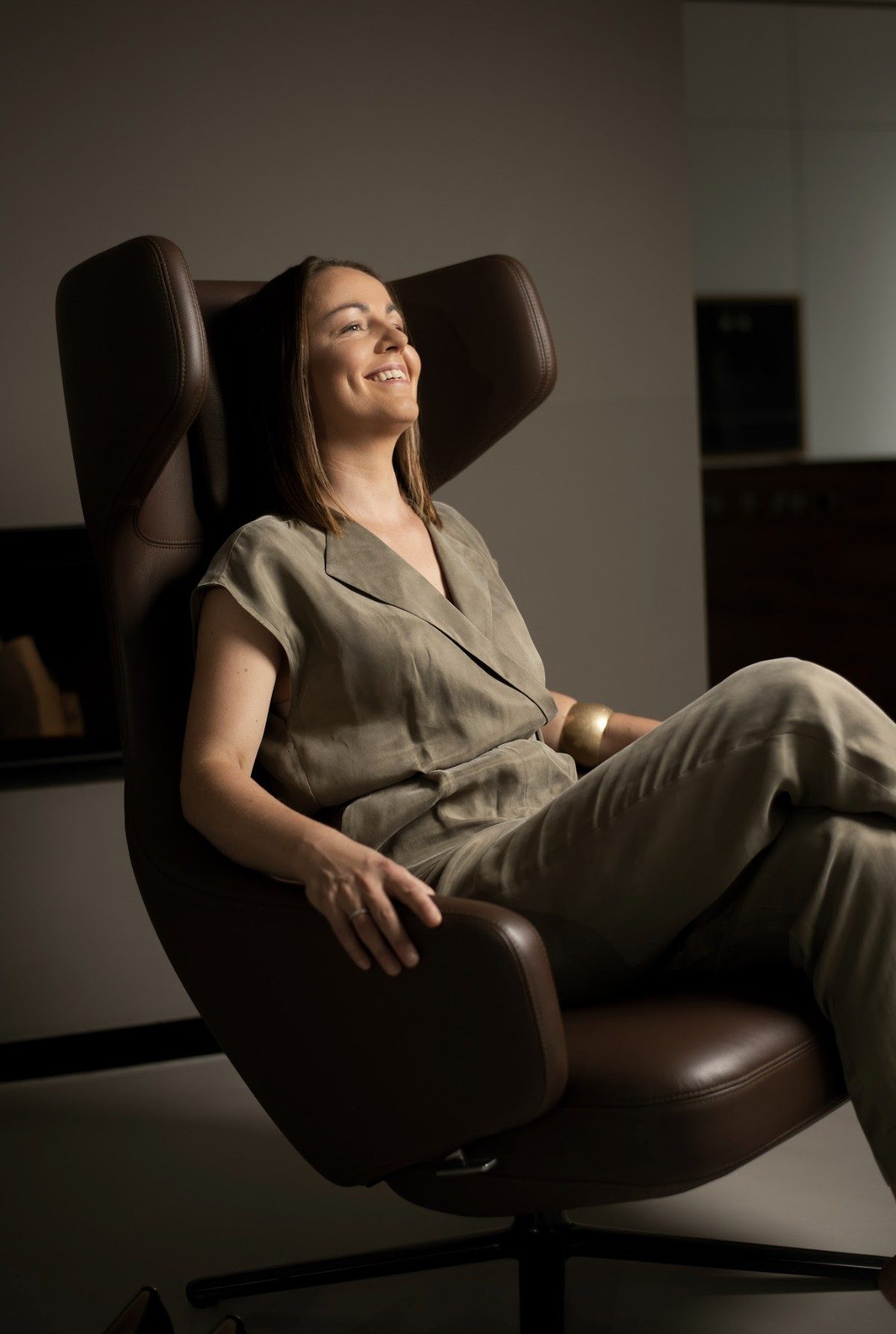 Businessportrait einer lachenden Frau im olivfarbenen Jumpsuit in einem braunen Ledersessel — Das Studiozwei, Werbefotograf München