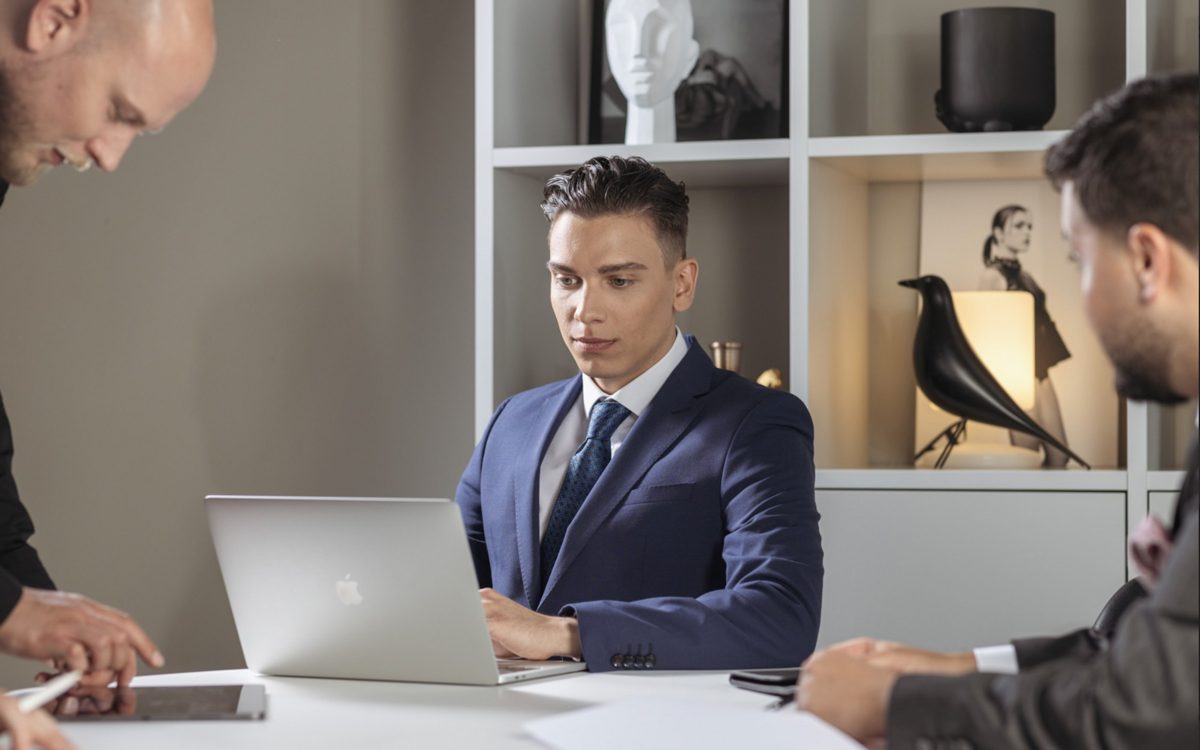 Drei Maenner in Anzuegen bei einer Besprechung an einem weissen Tisch mit Laptop — Das Studiozwei, Werbefotograf München