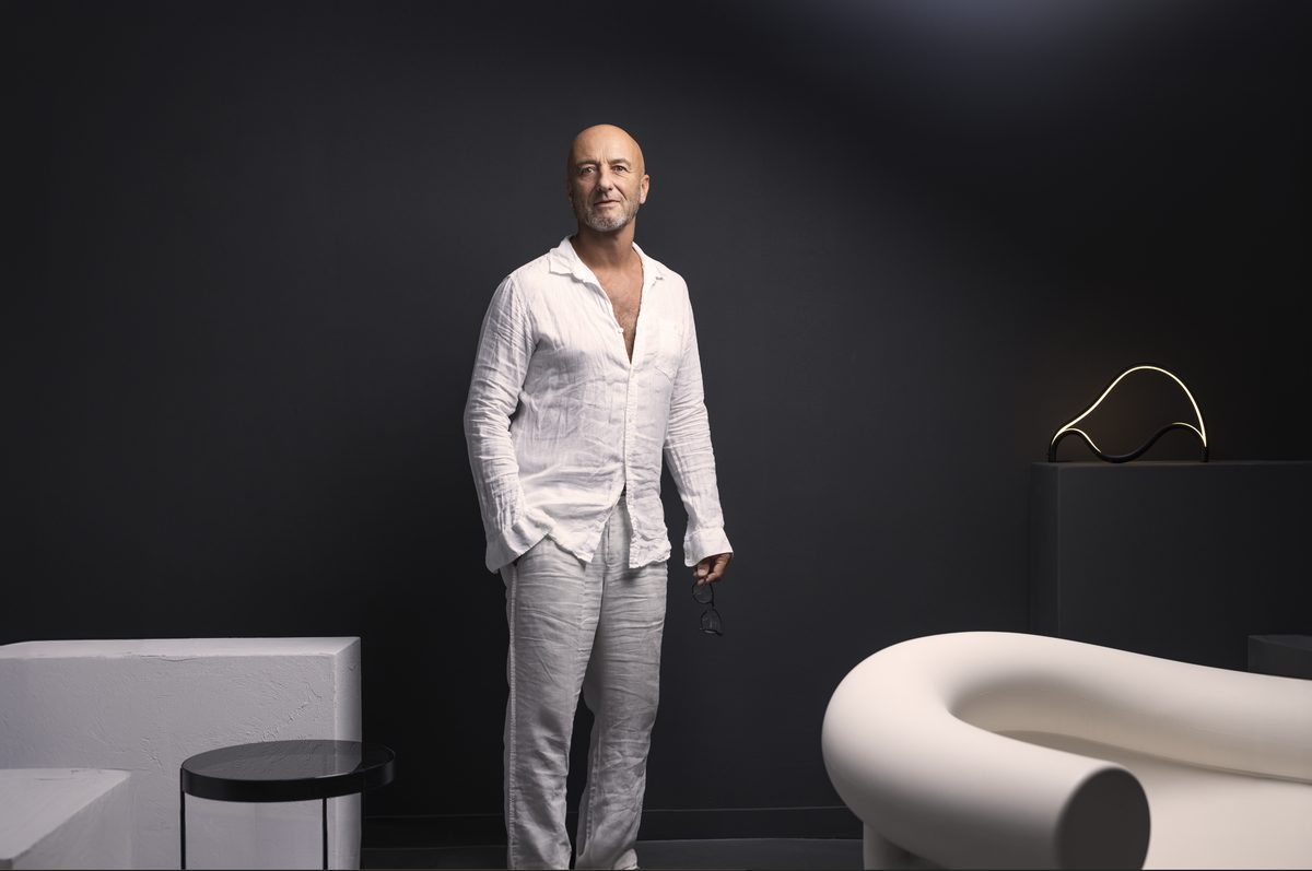 Mann in weissem Leinenhemd steht im dunklen Raum mit heller Sitzskulptur — Das Studiozwei, Werbefotograf München