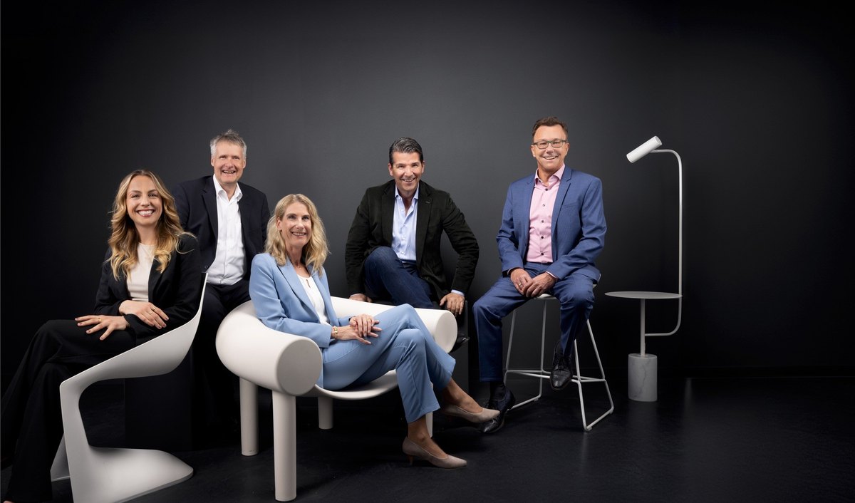 Fuenfkoepfiges Team in Business-Kleidung gruppiert um weisse Designmoebel vor dunklem Hintergrund — Das Studiozwei, Werbefotograf München