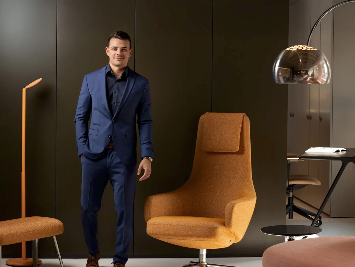 Businessportrait eines Mannes im blauen Anzug zwischen orangefarbenen Designsesseln — Das Studiozwei, Werbefotograf München