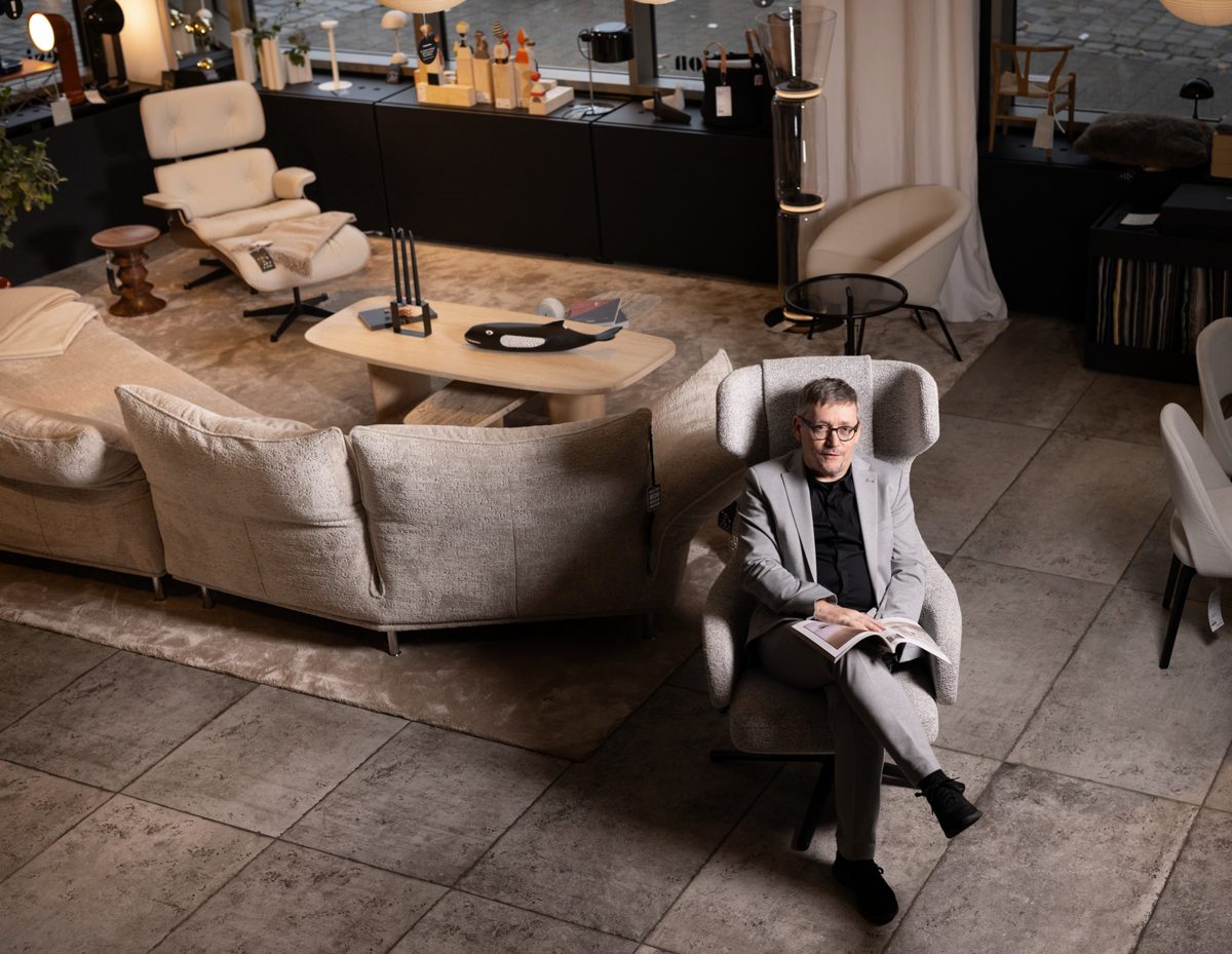 Mann im hellen Anzug sitzt mit Magazin in einem Sessel inmitten eines Moebel-Showrooms — Das Studiozwei, Werbefotograf München