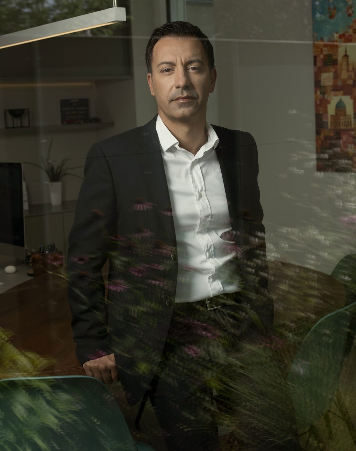 Businessportrait eines Mannes im schwarzen Anzug durch eine Glasscheibe mit Pflanzenspiegelung fotografiert — Das Studiozwei, Werbefotograf München